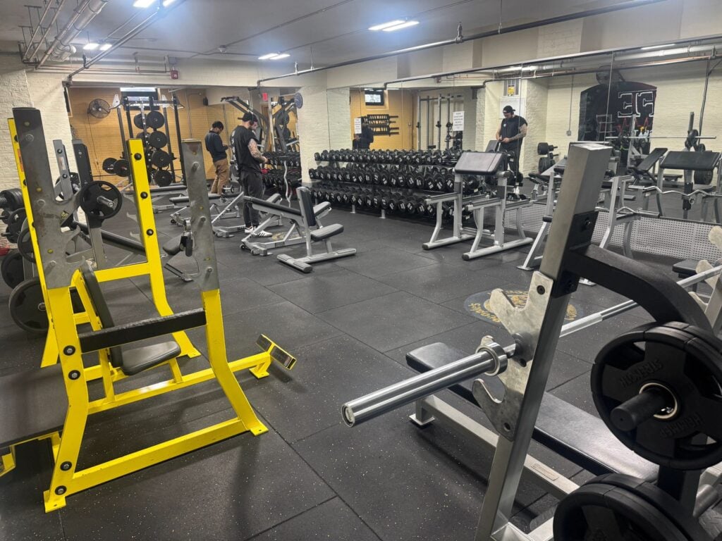 Members training in the AUCC weight room with dumbbell racks and squat racks